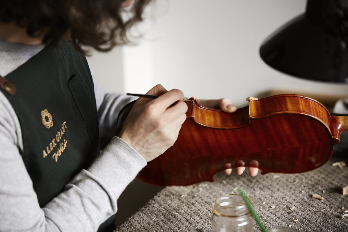 Image of a violin being revarnish by a Luthier, paintbrush in hand